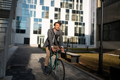Full-length front view of a young Caucasian businessman riding a bicycle on the way to work.