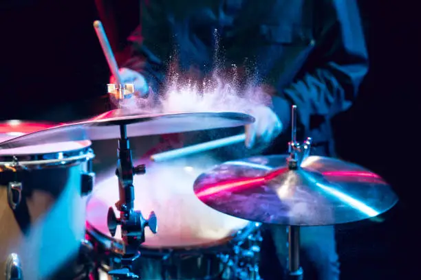 Drummer's rehearsing on drums before rock concert. Man recording music on drumset in studio. Neon light, trendy fluid colors. Concept of music, hobby, entertainment, fun. Close up, flying powder