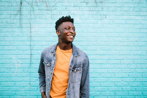 A smiling African American man stands in front of a blue wall wearing nice casual clothing.  Positive lifestyle portrait.  Shot in Portland, OR, USA.