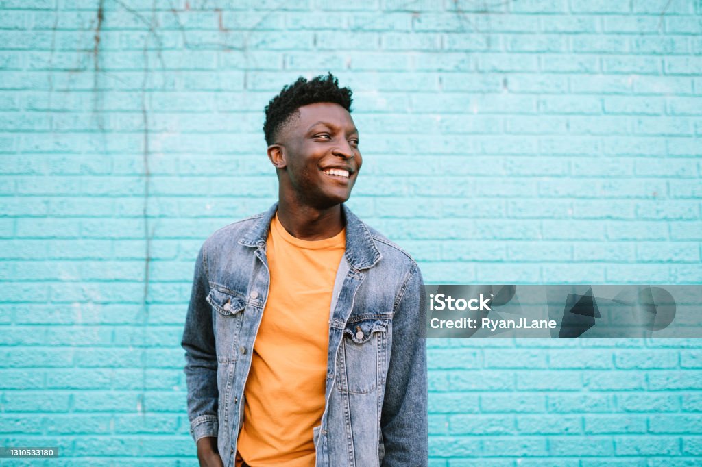 Cheerful Fashionable Adult Man in City Setting A smiling African American man stands in front of a blue wall wearing nice casual clothing.  Positive lifestyle portrait.  Shot in Portland, OR, USA. Men Stock Photo