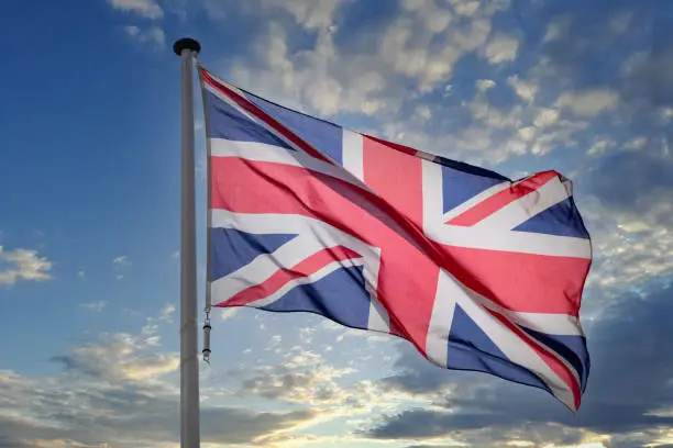 UK Britain flag, United Kingdom Great Britain and Northern Ireland national symbol on a flagpole waving against blue cloudy sky