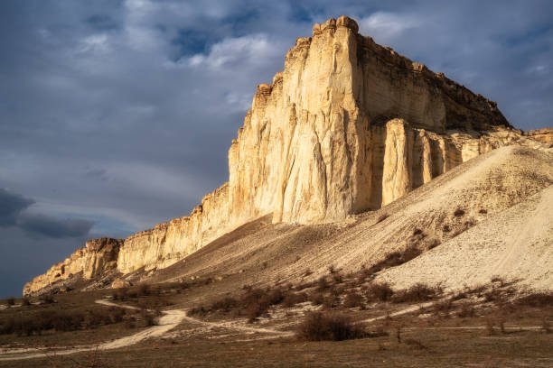 istock Beautiful white mountain peak lit by sun. White clouds and blue sky on background. Epic rock formation 1310537303