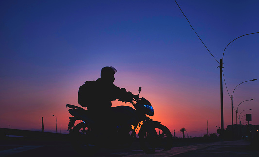 Night pizza delivery, man riding a motorcycle on the road at sunset. Selective focus