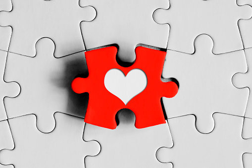 Heart shape on red puzzle piece in the middle of completely white jigsaw puzzle. Horizontal composition with enough copy space for your text.