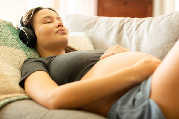 gente feliz escuchando música. una mujer embarazada relajándose, descansando en el sofá con auriculares. - filipino ethnicity audio fotografías e imágenes de stock