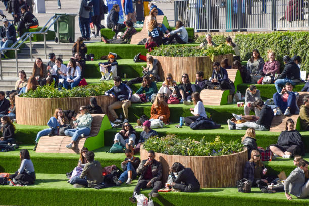 People sitting on green steps at Granary Square, King's Cross, London London, United Kingdom - April 2 2021: People enjoy the sunshine on the steps covered in artificial grass at Granary Square in King's Cross as the UK relaxes its lockdown restrictions. regents canal stock pictures, royalty-free photos & images