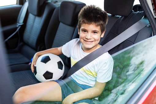 Happy little boy sitting on back seat of the car.He holding soccer ball .