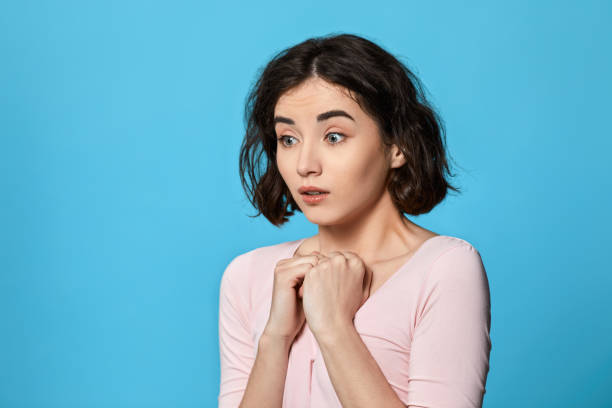 istock scared curly young brunette woman on blue background. 1310563591