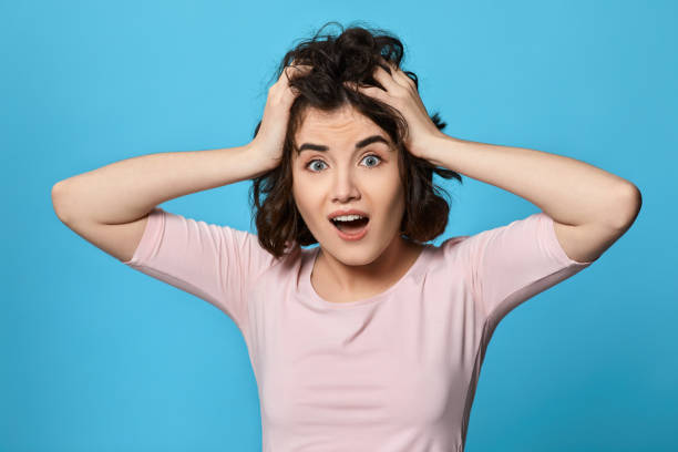 istock scared curly young brunette woman on blue background. 1310563610