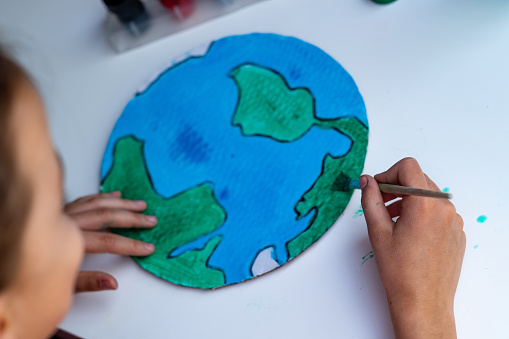 Girl painting planet Earth using watercolors and paintbrush