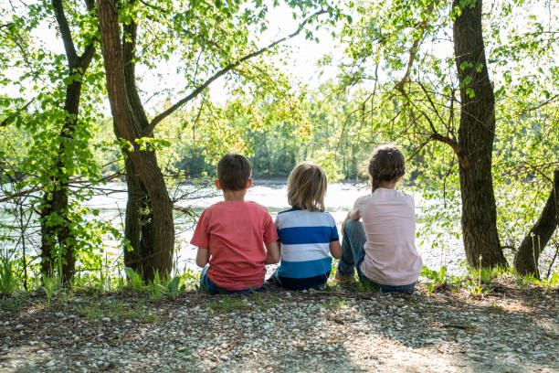 istock Rear view kids sitting at riverbank 1310566154