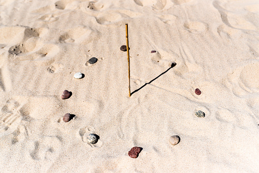 Sundial on the beach made of a stick and stones.