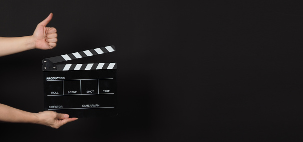 Hand is holding black clapperboard or movie slate and do like hand sign.It is used in film production and cinema,movies industry on black background.