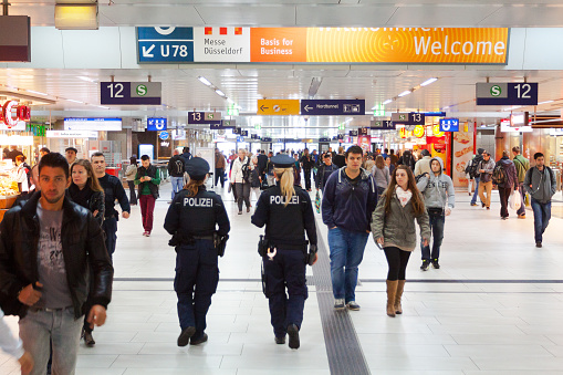 Two german police women are walking in hall of station Duesseldorf. Women are walking between commuters walking around. View along whole long corridor to exit