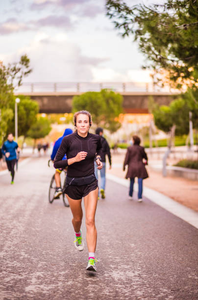ヘッドフォンでマラソンリスニング音楽のために外でカーディオを訓練する本当のランニング女性。スペインのライフスタイルの肖像画、スポーツの外の通り。 - marathon sport sports training city street ストックフォトと画像