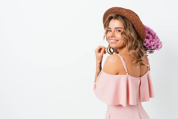 Cute young woman with bouquet fresh flowers wearing straw hat Cute young woman with bouquet fresh flowers wearing straw hat and pink dress smiling looking at camera while standing on white studio background with copy space. back shoulder tattoos for women pictures stock pictures, royalty-free photos & images