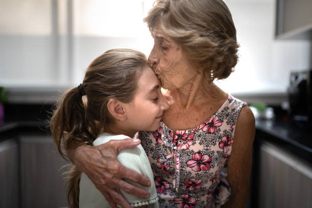 abuela besando la frente de su nieta en casa - grandmother generation gap senior adult granddaughter fotografías e imágenes de stock