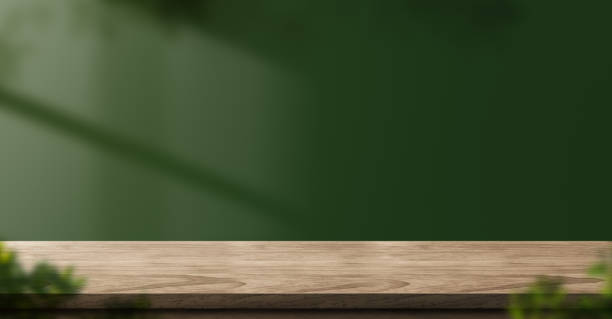 wood table green wall background with sunlight window create leaf shadow on wall with blur indoor green plant foreground.panoramic banner mockup for display of product.eco friendly interior concept stock photo