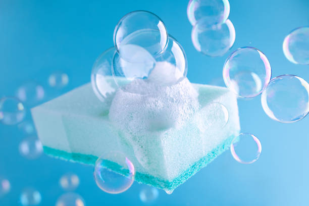 Light Blue cleaning sponge with foam and soap bubbles on blue background. Housework or cleaning services of home.Cleaning supplies concept.