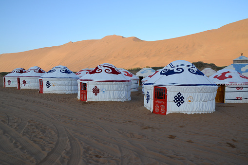 Mongolian Yurts surrounded by huge sand dunes in Badain Jaran desert. This desert is home to some of the tallest stationary dunes on Earth, with some reaching a height of more than 500 meters. The desert also features over 100 spring-fed lakes that lie between the dunes, some of which are fresh water while others are extremely saline. It is a subsection of the Gobi desert. Inner Mongolia, China.