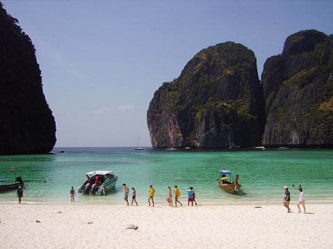 Tourists walking on the white sand beach at famous Maya Bay in Phi Phi Le island, Thailand