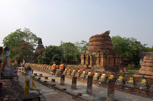 View of ancient stupa ruin rounded by crosslegged buddhas at the Wat Yai Chai Mongkhon in Ayutthaya, Thailand