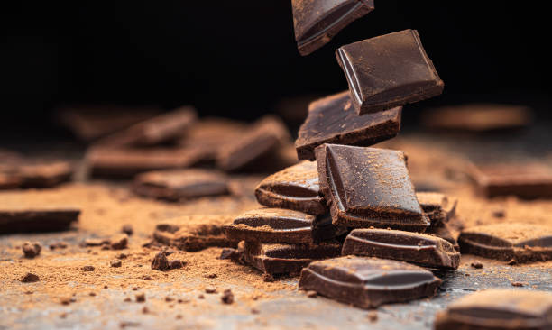 Falling broken chocolate bars on black background Falling broken chocolate bars on black slate background with cocoa powder, stack of dark chocolate pieces chocolate stock pictures, royalty-free photos & images