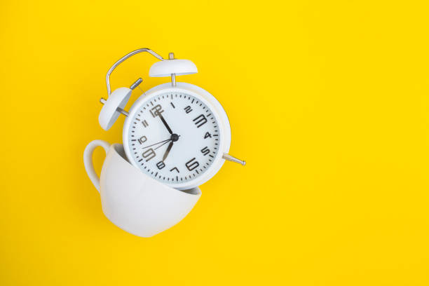 istock White alarm clock and  white cup on the yellow background 1310595073