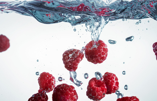 Raspberries falling into water with splashes and air bubbles. Selective focus.