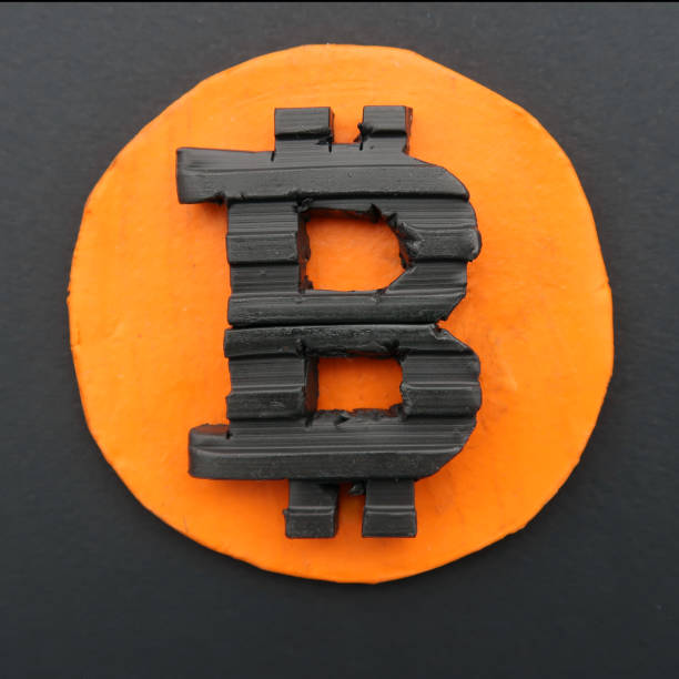 Black Bitcoin symbol on a circular golden orange base. Real three dimensional model flat lay