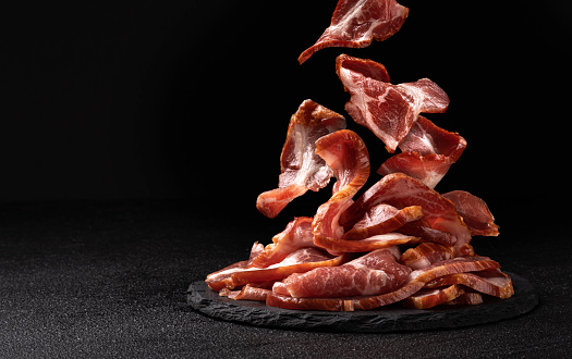 Sliced bacon on black background, raw ham strips, with copy space