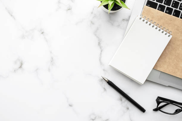 istock White marble office desk table with blank notebook, pen and supplies. Top view with copy space, flat lay. 1310604728