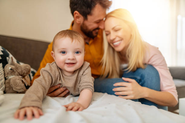 Young parents and their little cute baby boy relaxing on sofa stock photo