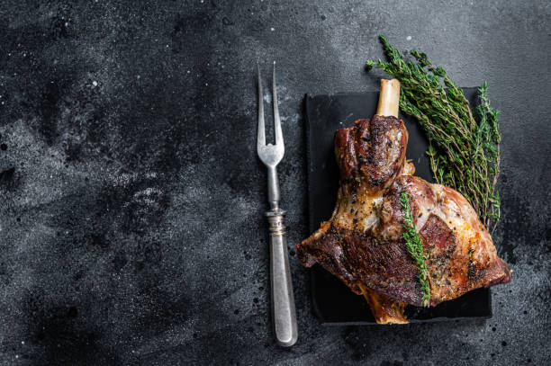 istock Oven Roasted lamb mutton whole leg with thyme. Black background. Top view. Copy space 1310613432