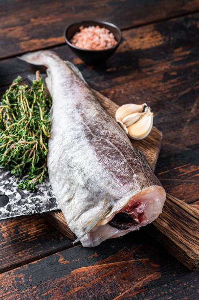 istock Fresh Raw cod or codfish fish on wooden board with cleaver. Dark Wooden background. Top view 1310613520