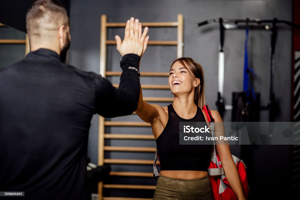 Young Caucasian woman going to the gym Happy young Caucasian woman arriving to the gym, high fiving her fitness instructor and smiling Fitness Instructor Stock Photo