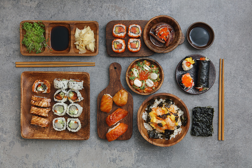 Sushi and sushi roll set (Sake nigiri sushi, notate nigiri sushi, Philadelphia rolls, spicy tuna roll, scallop roll). Tuna tataki. Raw scallop rice bowl with mango, spicy mayo, tobiko caviar and nori chips. Gunkan set. Temaki. Flat lay top-down composition on concrete background.