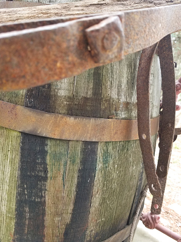 Antique wooden barrel with metal stays.  Hanging from the barrel are parts and pieces of various farm equipment, traps, and tools.