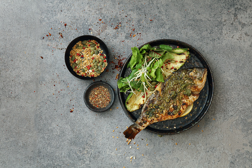 Barbecued sea bream with pesto dressing, wild rocket salad and grilled zucchini. Flat lay top-down composition on concrete background.