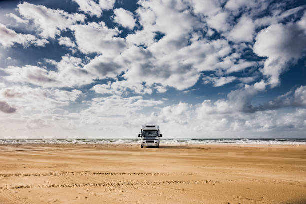 Young woman with a straw hat and backpack is watching the view of the sea and walking next to her camper