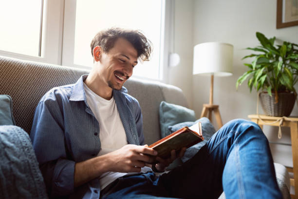 istock Cheerful young man reading a book at home 1310623134