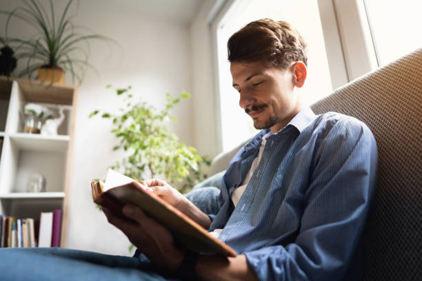 istock Smiling young man reading a book at home 1310623196