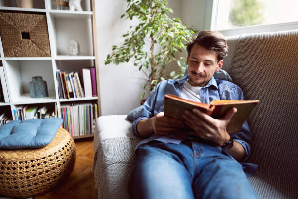 istock Happy young man lying on the sofa and reading a book 1310623217