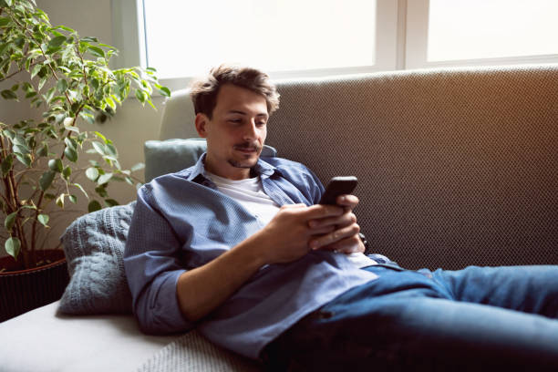 istock Young man lying on the sofa and using smart phone 1310623242