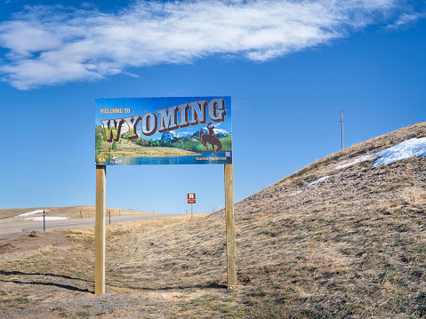 Cheyenne, WY, USA - April 2, 2021: Welcome to Wyoming - road sign with some stickers added by travelers, highway 85 in early spring scenery.