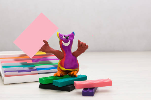 A plasticine figure resembling a cat on a light background holds a clean empty table. Blank sheet. Copy space