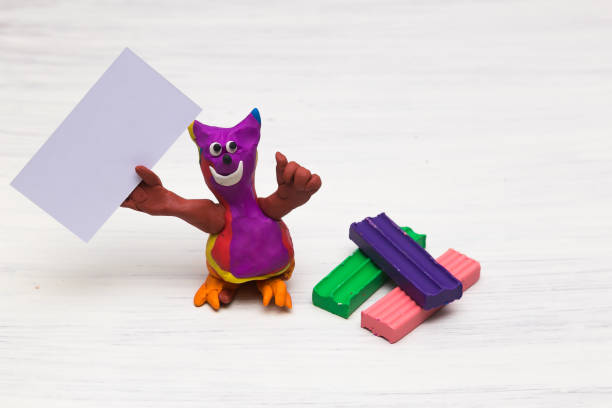 istock A plasticine figure resembling a cat on a light background holds a clean empty table. Blank sheet. Copy space 1310634586