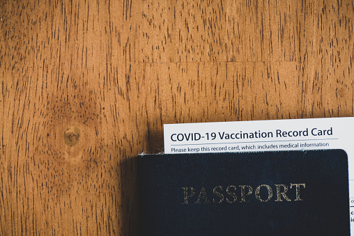 A Covid-19 vaccination record card is tucked inside a well-used passport, ready to travel again