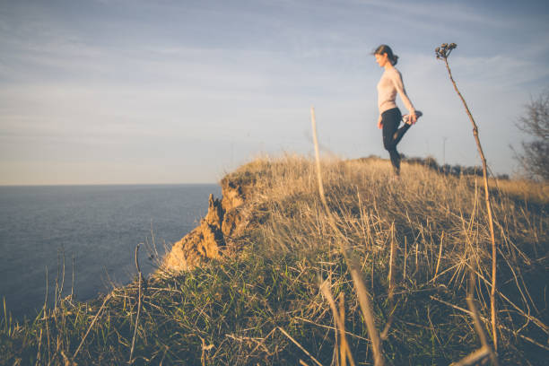 Fit and active danish female trail runner dressed in fitness clothing enjoying the spectacular view at the Greater Belt Bridge (Storebæltsbroen) in Denmark, while stretching on top of a sea cliff in evening sun.