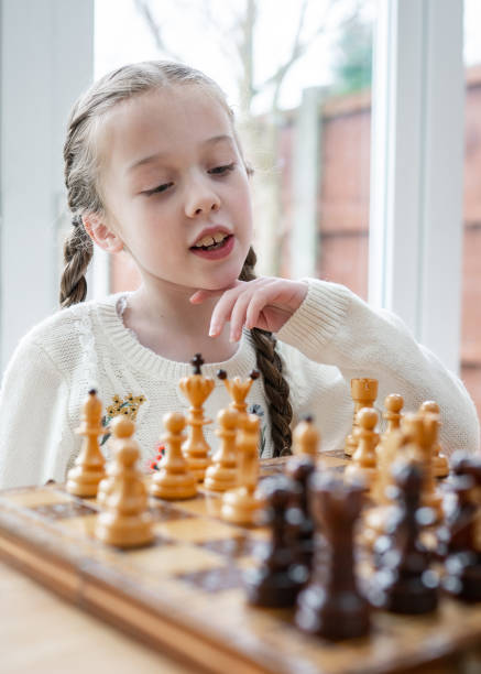 美しいかわいい天才の子供の若い女の子は、チェスボードの子供に木片でチェスゲーム戦略をプレイし、キングとクイーンとの計画移動を集中 - queens head ストックフォトと画像